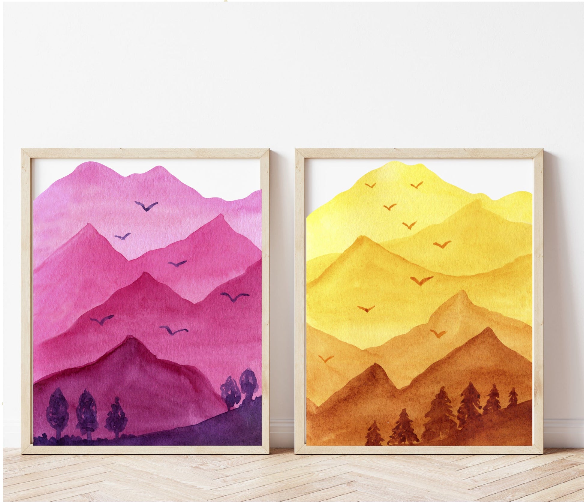 Two framed artworks of mountains in pink and yellow on a white wall.